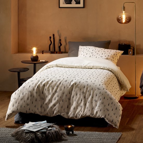 Lit fait avec housse de couette en tissu crème à motif de petits arbres noirs. Robuste et d'ambiance.