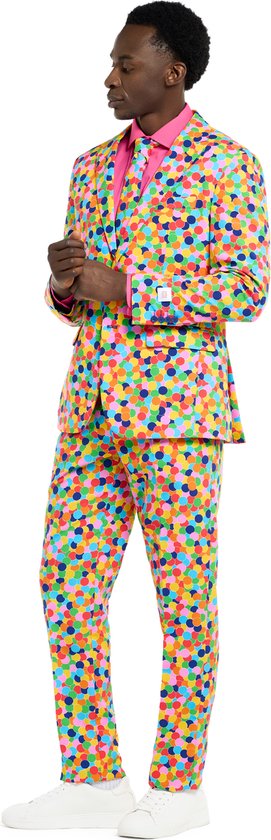 Man in een veelkleurig pak met confettiprint en roze shirt, zij-aanzicht.