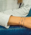 Twee zilverkleurige armbanden om een arm. Eén met ovale schakels en bolletjes, de andere met een fijne ketting met bolletjes.
