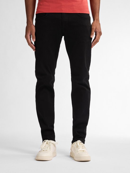 Model draagt een zwarte slim fit jeans en een rood t-shirt, bekeken vanaf de voorzijde.