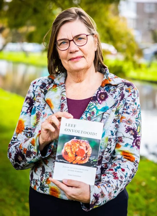 Een vrouw met een kleurrijke jas met bloemenprint, die een boek vasthoudt met de titel 'Leef onvoltooid!'.
