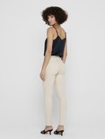 Model met een navy top en beige skinny jeans, gezien vanaf de zijkant.