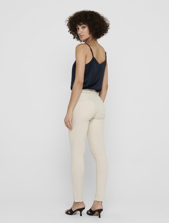 Model met een navy top en beige skinny jeans, gezien vanaf de zijkant.