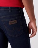 Detail van donkerblauwe Wrangler jeans: achterzak met bruin logo en stiksels.
