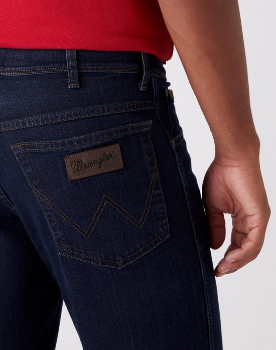 Detail van donkerblauwe Wrangler jeans: achterzak met bruin logo en stiksels.