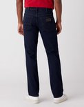 Man met donkerblauwe Wrangler jeans met bruine stiksels, witte sneakers.