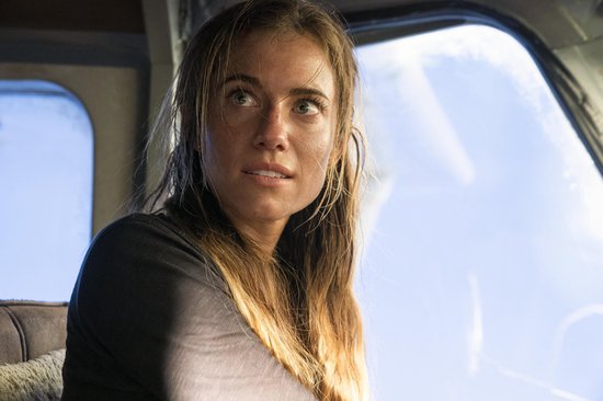 Close-up van een vrouw met bruin haar in een zwart T-shirt, met een schram op haar wang, die naar de zijkant kijkt.