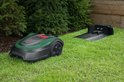 Groene en zwarte robotmaaier naast een laadstation in een tuin.