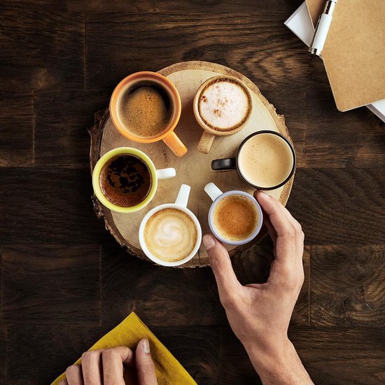 Hand pakt een kopje espresso van een boomstronk met zes gevulde kopjes.