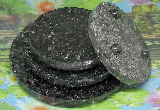Een stapel van vier ronde, zwarte schotels met schungiet snippers. De bovenste schotel is opgelicht en toont de bolletjes aan de onderkant.