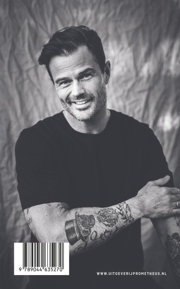 Zwart-wit portret van een man met tatoeages op zijn armen, lachend naar de camera.