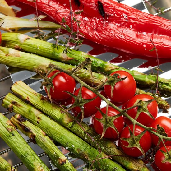 Close-up van gegrilde groenten en kruiden op een grillrooster. Groene asperges, cherrytomaatjes en rode paprika.