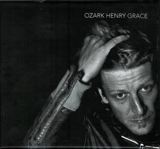 Zwart-wit portret van Ozark Henry die aan zijn haar zit. Titel bovenaan.
