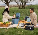 Jackery Explorer 500 powerstation op een picknickkleed met een blauw koelbox en fruit.