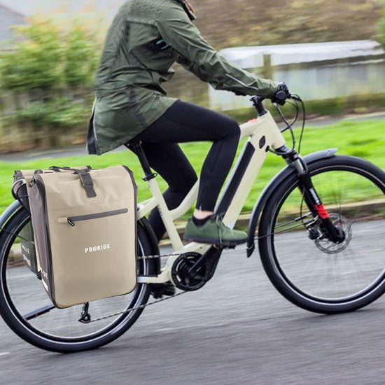 Beige dubbele fietstas aan de achterkant van een elektrische fiets, bereden door een persoon in een groene jas.