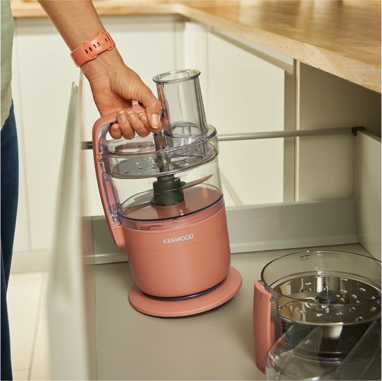 Rosekleurige Kenwood keukenmachine met deksel, handvat en mes in de transparante kom.