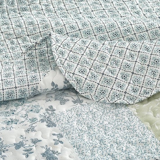 Close-up van een blauwgroene quilt met patchwork van bloemenprints en ruitpatronen.