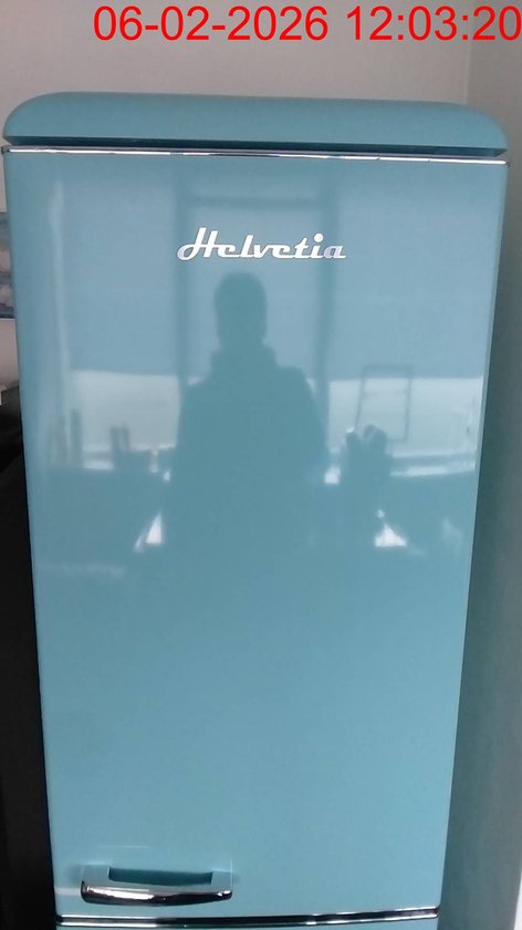 Hemelsblauwe Helvetia koelkast met zilveren handgreep en logo. Spiegelt een persoon.