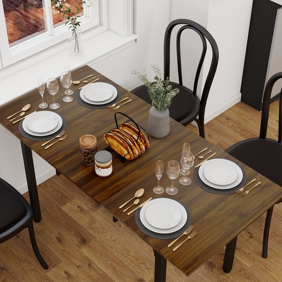 Eettafel met walnoothouten blad, gedekt voor vier personen met gouden bestek, witte borden en wijnglazen.