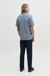 Man staat met zijn rug naar de camera in een effen blauw poloshirt en jeans.
