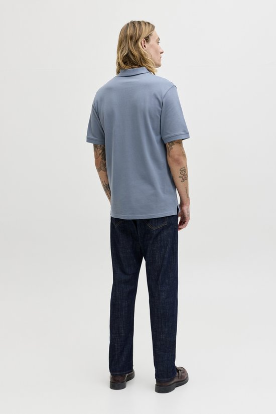Man staat met zijn rug naar de camera in een effen blauw poloshirt en jeans.