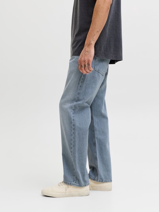 Blauwe jeans met wijde pijpen, gedragen door een man met tatoeages op zijn arm.