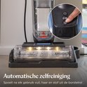 Close-up van de borstelkop van een stofzuiger met ledverlichting, met een hand die de zelfreinigingsknop indrukt.
