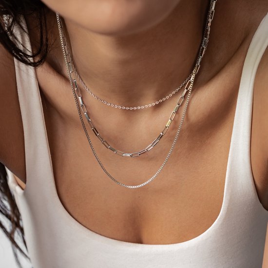 Een model draagt een zilverkleurige, gelaagde ketting met fijne schakels, paperclip schakels en een vensterketting.