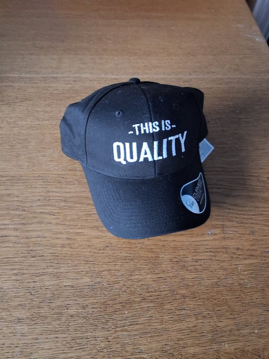 Zwarte pet met de tekst "THIS IS - QUALITY" in witte letters.