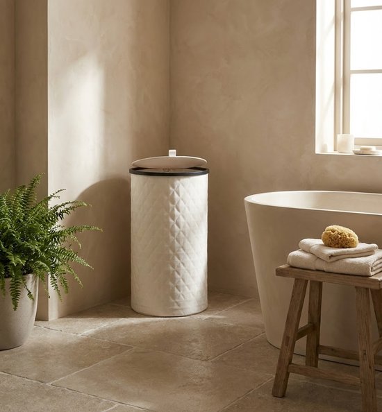 Crèmekleurige MAZAZU wasmand met ruitpatroon in een badkamer, naast een bad en een plant.