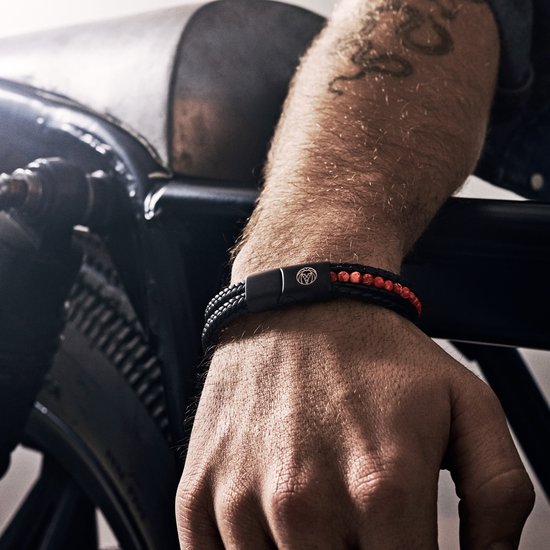 Man met tatoeage draagt een zwarte gevlochten leren armband met rode kralen en zwarte magneetsluiting.