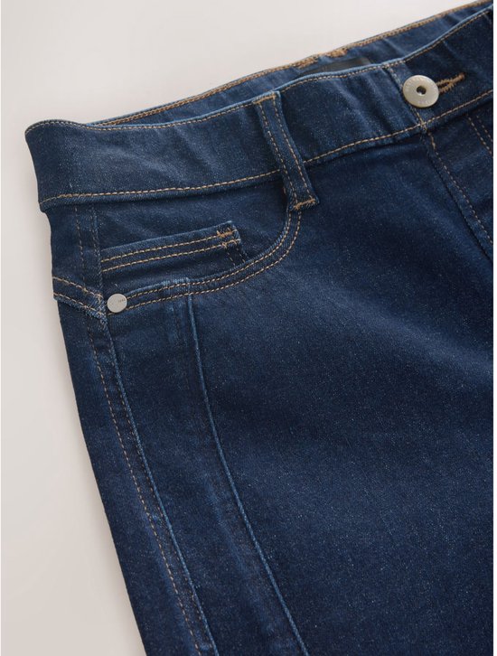 Detail van de tailleband en zak van een donkerblauwe spijkerbroek met knoopsluiting.