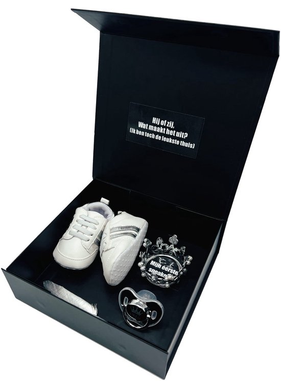 Zwarte geschenkdoos met witte babyschoentjes, een kroontje en een speen met tekst. De tekst op het kroontje is 'Mijn eerste spuugdoekjes'.