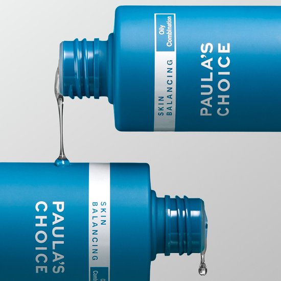 Twee blauwe Paula's Choice flessen, een druppel vloeistof valt van de bovenste fles op de onderste.