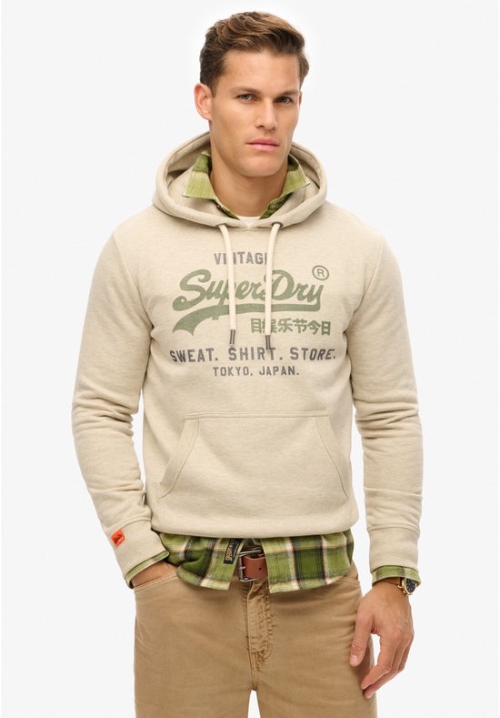 Sweat à capuche beige avec inscription "Vintage Super Dry Sweat. Shirt. Store. Tokyo, Japan.". Porté par un homme avec une chemise à carreaux verts.