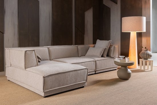 Lichtbeige modulaire bank met kussens, bijzettafel en grote staande lamp.