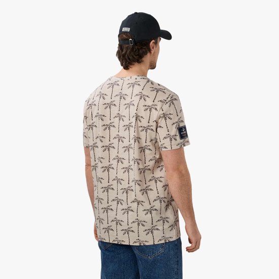 Man van achteren, draagt beige T-shirt met palmbomenprint, spijkerbroek en zwarte pet.