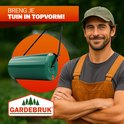 Man met bruine overall en groene pet, glimlachend naast een groene Gardebruk tuinwals.