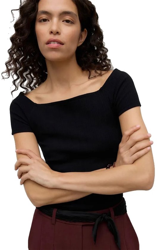 Model met zwarte, aansluitende top met off-shoulder hals, korte mouwen.