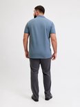 Man met baard, achterkant van een blauw poloshirt en grijze broek.