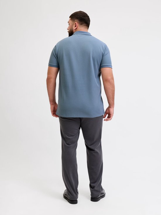 Man met baard, achterkant van een blauw poloshirt en grijze broek.