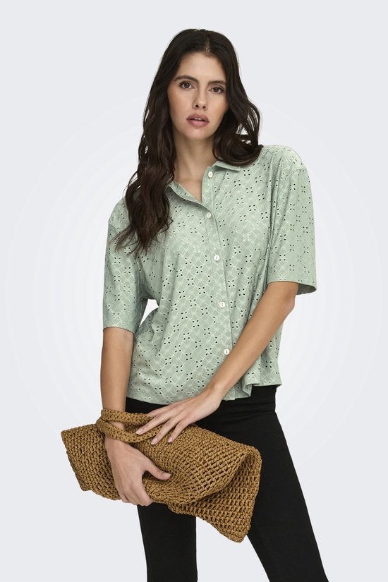 Model met lichtgroene blouse met korte mouwen, broderie anglaise en bruine tas.