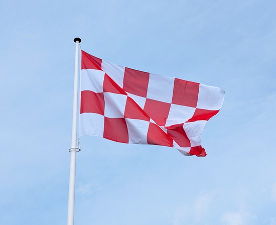 Rood-wit geblokte vlag wapperend aan een witte paal tegen een blauwe lucht.