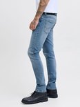 Man met tatoeages in een lichtblauwe slim fit jeans, zwarte schoenen en een grijze T-shirt.