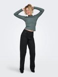 Model met blond haar draagt een grijze coltrui met lange mouwen, geribde textuur, gegolfde kraag en een zwarte broek.