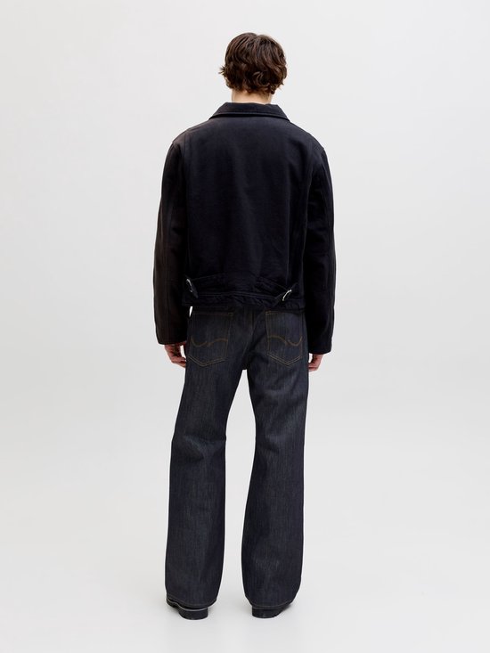 Model van achteren gezien met zwarte jas en donkere jeans met wijd uitlopende pijpen.
