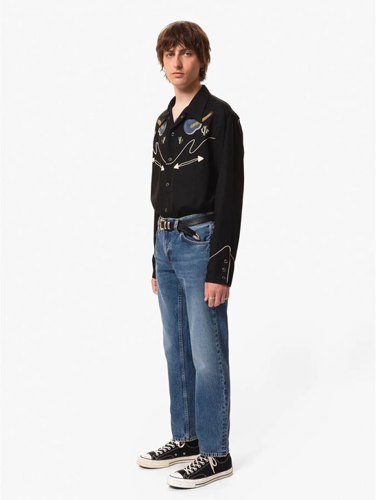 Man in spijkerbroek en zwart shirt met geborduurde details