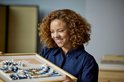 Femme aux cheveux roux bouclés regardant une mosaïque LEGO Art 'La Grande Vague' encadrée.