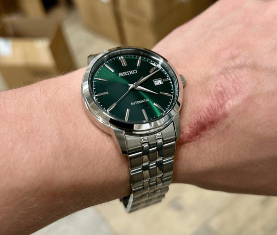 Seiko herenhorloge met smaragdgroene wijzerplaat en zilverkleurige metalen band, gedragen op een arm.