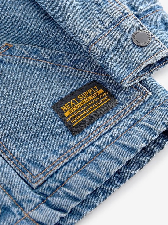 Blauw denim jack met label "NEXT SUPPLY ESTABLISHED 1982".